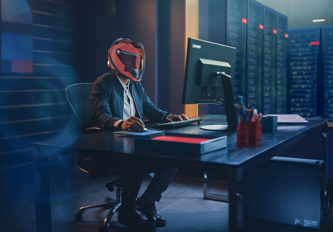 Professional sitting at a desk in a data cccenter with a helmet on.